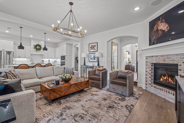 living room featuring arched walkways, recessed lighting, a fireplace, wood finished floors, and crown molding