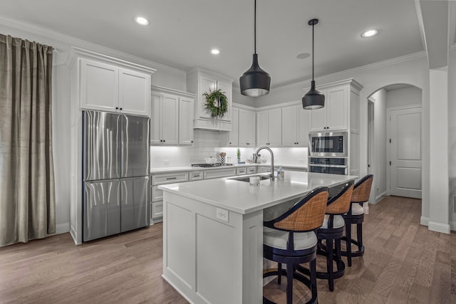 kitchen with light wood finished floors, arched walkways, decorative backsplash, stainless steel appliances, and a sink