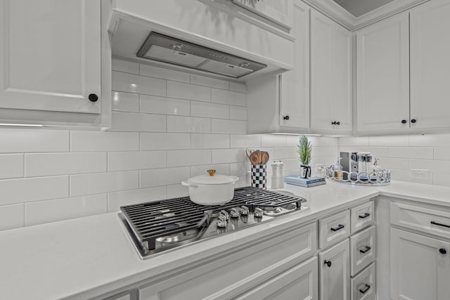 kitchen with tasteful backsplash, light countertops, under cabinet range hood, stainless steel gas stovetop, and white cabinetry