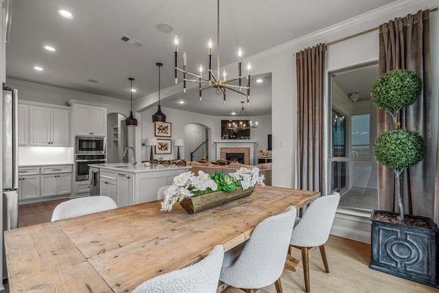 dining area featuring arched walkways, crown molding, a fireplace, visible vents, and light wood-style flooring