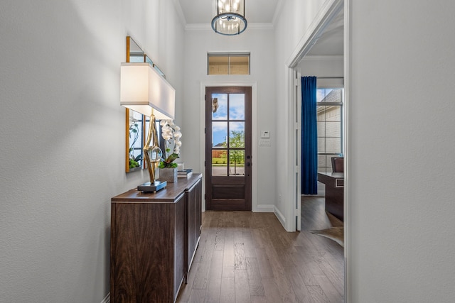 entryway featuring baseboards, wood-type flooring, a notable chandelier, and crown molding