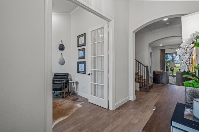 entryway with arched walkways, wood finished floors, baseboards, stairs, and crown molding