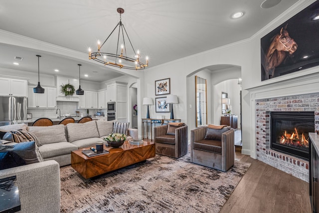 living area with arched walkways, wood finished floors, visible vents, ornamental molding, and a brick fireplace