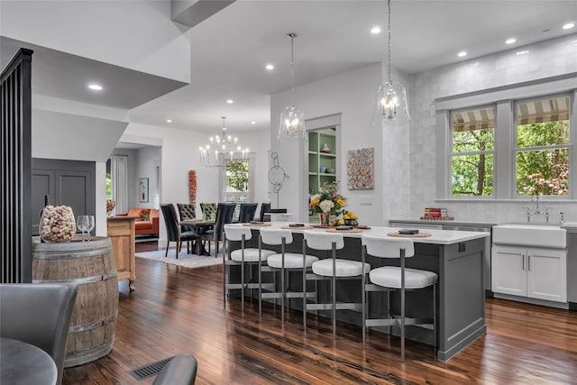 kitchen with dark wood-style floors, a breakfast bar, a center island, light countertops, and a sink