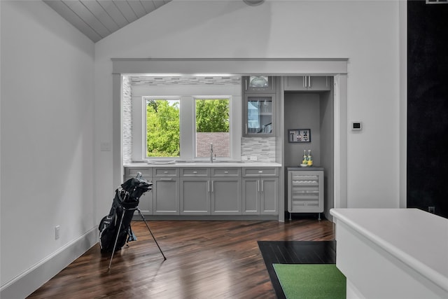 interior space with lofted ceiling, decorative backsplash, dark wood-type flooring, a sink, and beverage cooler