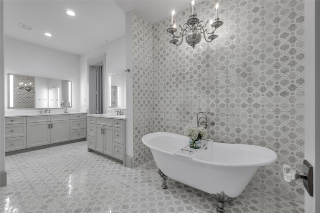 full bath with two vanities, a notable chandelier, a freestanding bath, a sink, and recessed lighting