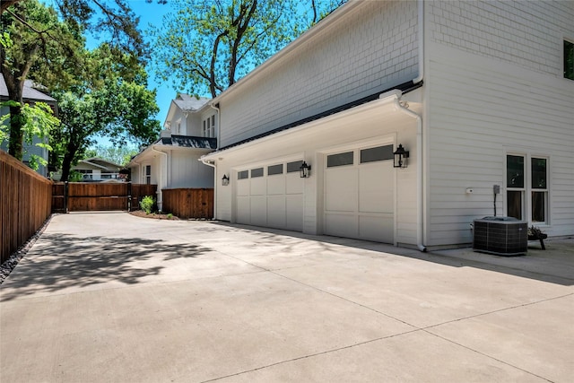 view of side of home featuring an attached garage, fence, central AC, and concrete driveway