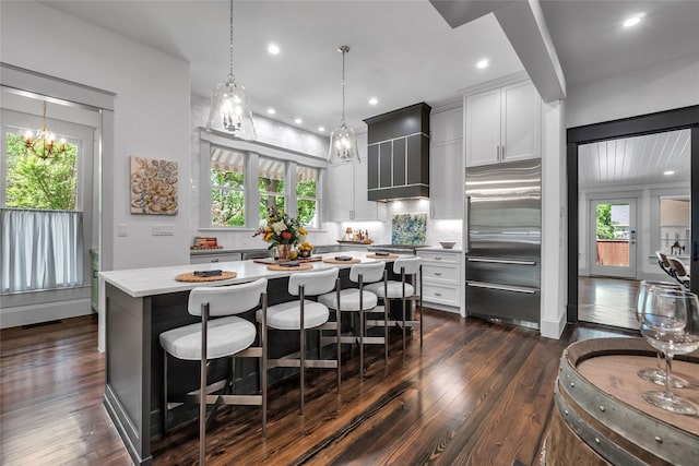 kitchen featuring built in fridge, light countertops, dark wood-type flooring, a kitchen island, and wall chimney exhaust hood