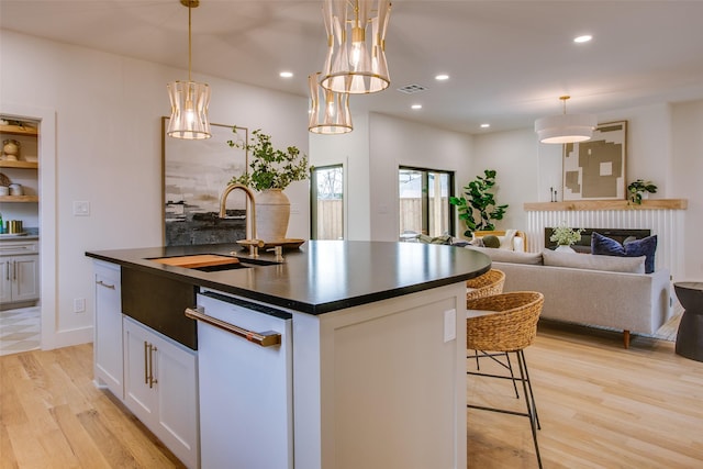 kitchen with a sink, visible vents, light wood-type flooring, an island with sink, and dark countertops