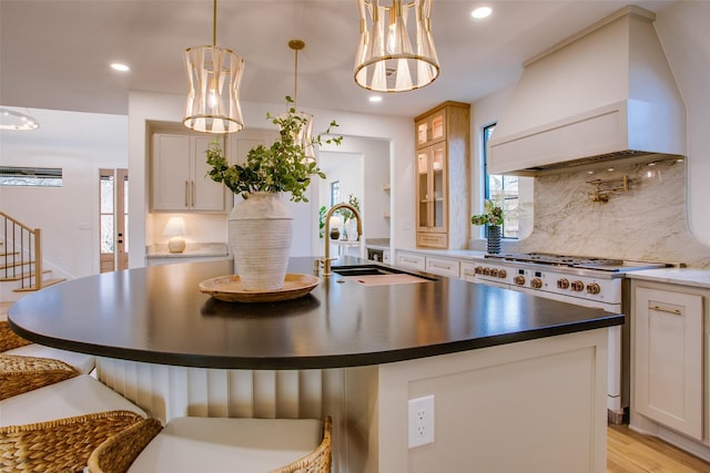 kitchen with stainless steel stove, a sink, custom exhaust hood, dark countertops, and a center island with sink