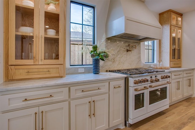 kitchen with glass insert cabinets, double oven range, light stone counters, and custom exhaust hood