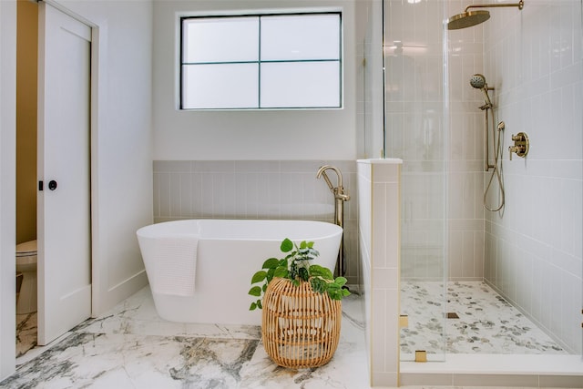 bathroom with marble finish floor, tile walls, toilet, a stall shower, and a freestanding tub