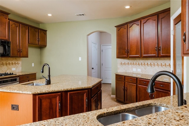 kitchen with light stone countertops, visible vents, black microwave, and a sink