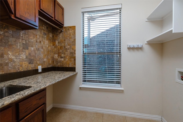 kitchen with built in desk, light tile patterned floors, decorative backsplash, baseboards, and light stone countertops