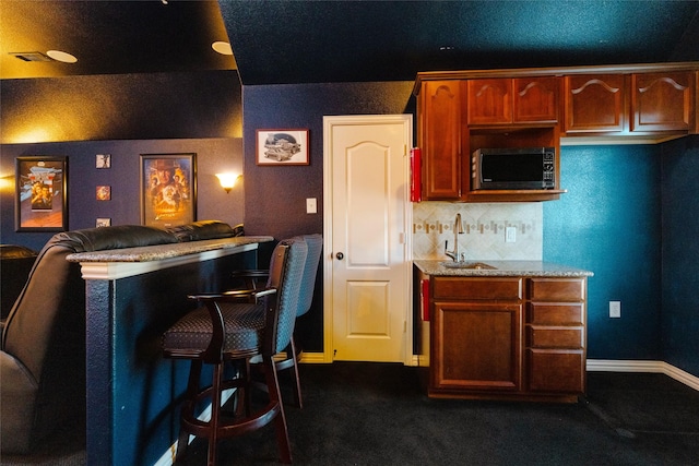 kitchen featuring a sink, decorative backsplash, baseboards, and light stone countertops