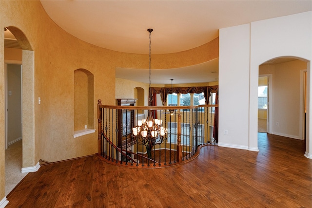 corridor featuring an upstairs landing, arched walkways, baseboards, and wood finished floors