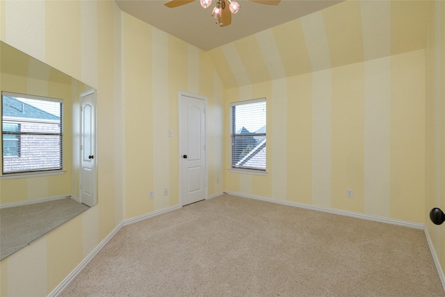 carpeted empty room featuring ceiling fan, baseboards, a towering ceiling, and wallpapered walls