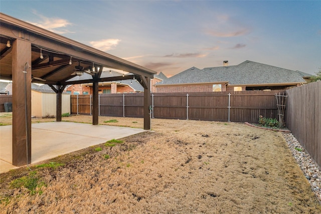 yard at dusk featuring a patio, a ceiling fan, and a fenced backyard