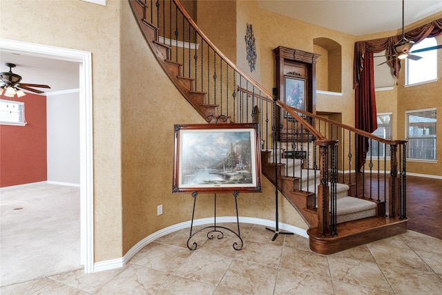 stairs with carpet flooring, baseboards, a towering ceiling, and ceiling fan