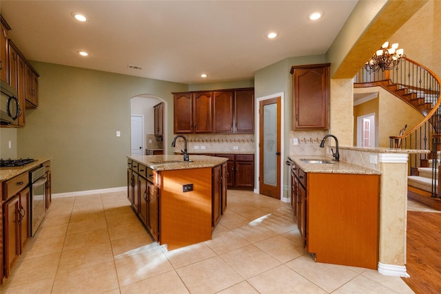 kitchen featuring light stone counters, visible vents, a center island with sink, and a sink