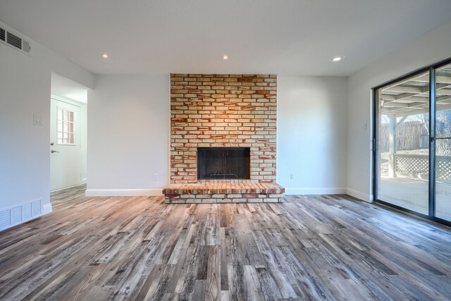 unfurnished living room featuring a brick fireplace, baseboards, wood finished floors, and recessed lighting