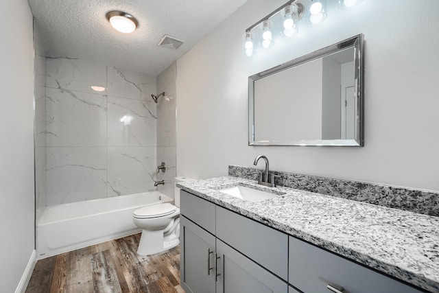 bathroom with a textured ceiling, toilet, wood finished floors, vanity, and visible vents