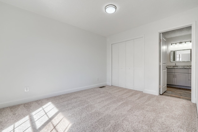 unfurnished bedroom featuring a sink, a closet, carpet flooring, and baseboards