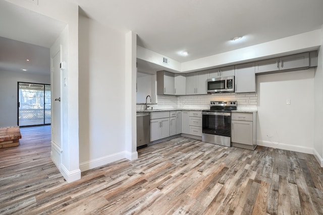 kitchen featuring light wood finished floors, visible vents, appliances with stainless steel finishes, gray cabinets, and backsplash