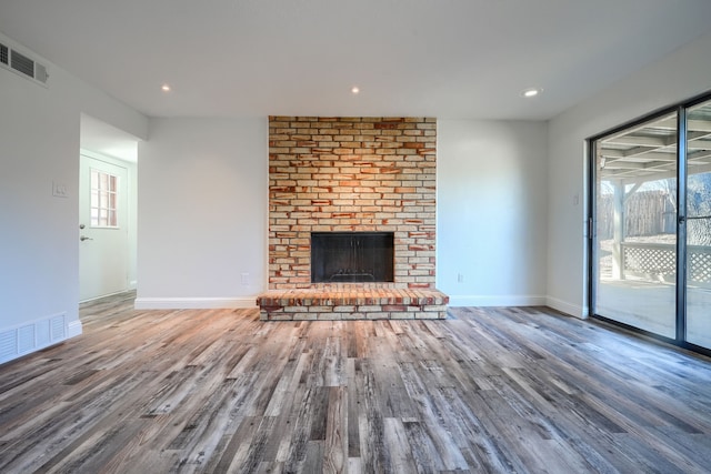 unfurnished living room with a brick fireplace, a healthy amount of sunlight, visible vents, and wood finished floors