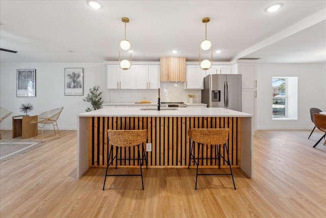 kitchen with a sink, white cabinetry, light countertops, a large island, and stainless steel fridge