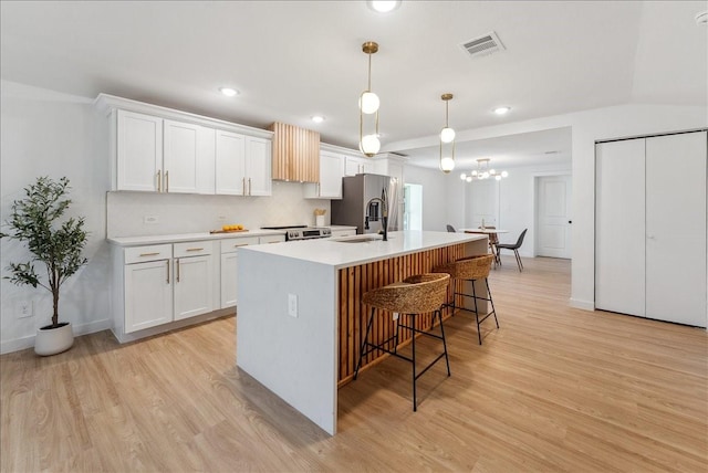 kitchen with a center island with sink, stainless steel refrigerator with ice dispenser, a breakfast bar area, visible vents, and white cabinets