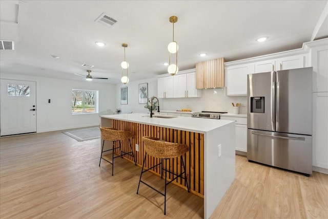 kitchen with visible vents, a breakfast bar area, stainless steel appliances, light wood-style floors, and a sink