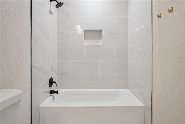 bathroom with toilet, shower / bathtub combination, and a textured wall