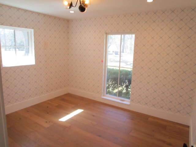 empty room featuring an inviting chandelier, wood finished floors, baseboards, and wallpapered walls