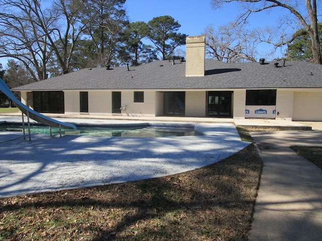 rear view of house with brick siding, a patio, a chimney, roof with shingles, and an outdoor pool