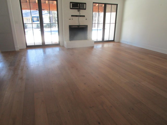 unfurnished living room with baseboards, a healthy amount of sunlight, a fireplace, and hardwood / wood-style floors