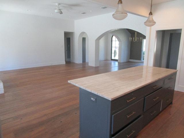 kitchen with arched walkways, a ceiling fan, open floor plan, dark wood-type flooring, and light countertops