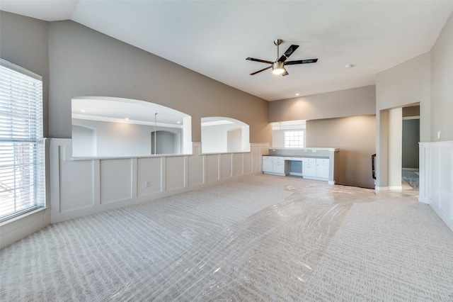 unfurnished living room with lofted ceiling, carpet flooring, a ceiling fan, and a decorative wall