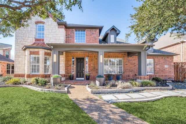 view of front of home with brick siding, a porch, a shingled roof, stone siding, and a front lawn