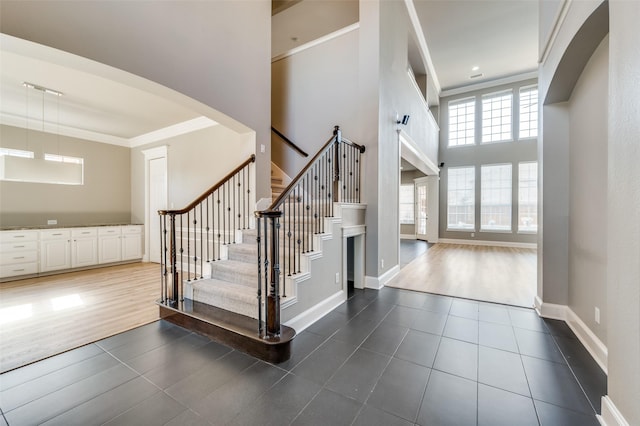 entryway featuring ornamental molding, a towering ceiling, baseboards, and dark tile patterned floors