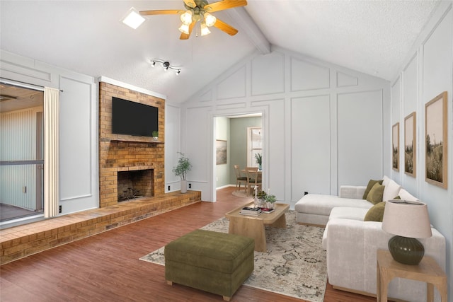 living area featuring vaulted ceiling with beams, a fireplace, wood finished floors, and a decorative wall