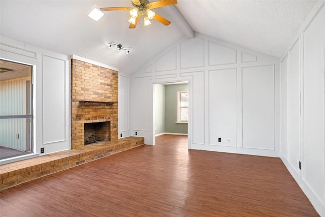 unfurnished living room featuring vaulted ceiling with beams, a decorative wall, a fireplace, wood finished floors, and a ceiling fan