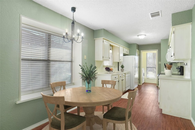 dining room featuring baseboards, visible vents, dark wood-style floors, a textured ceiling, and a chandelier