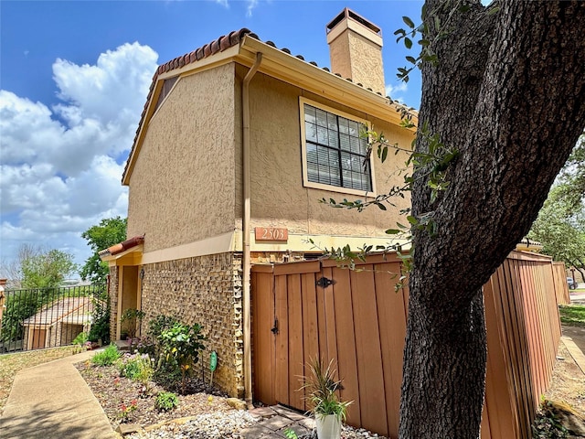 view of side of property featuring stucco siding, a tile roof, a chimney, and fence