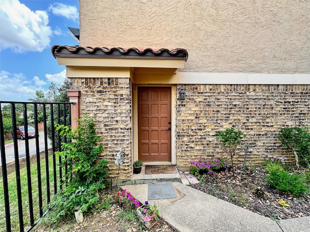 property entrance featuring a tiled roof, stone siding, and stucco siding