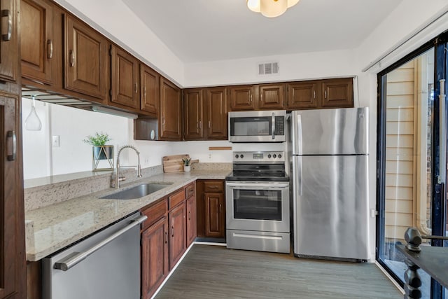 kitchen with visible vents, light stone countertops, appliances with stainless steel finishes, wood finished floors, and a sink