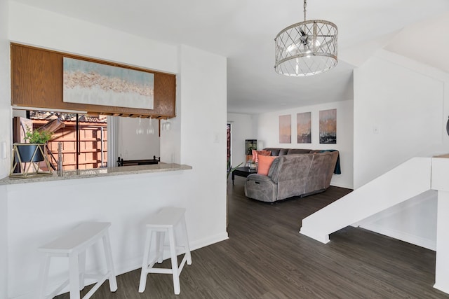 kitchen featuring a notable chandelier, a kitchen breakfast bar, baseboards, and dark wood-style flooring