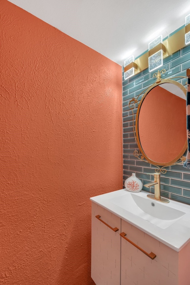 bathroom featuring decorative backsplash, a textured wall, and a sink