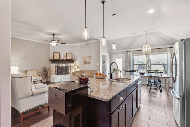 kitchen featuring light stone counters, stainless steel appliances, crown molding, a fireplace, and a sink