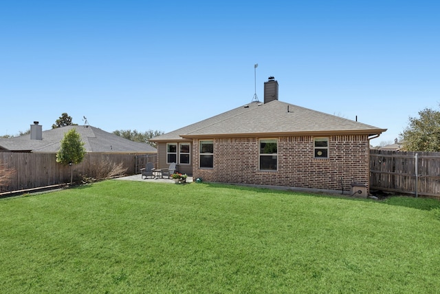 rear view of house featuring a lawn, a fenced backyard, roof with shingles, a patio area, and brick siding